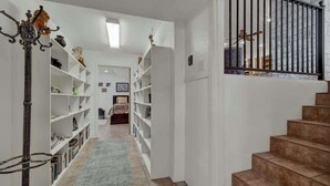 A narrow hallway with white shelving units on both sides, leading to a staircase with a black railing.
