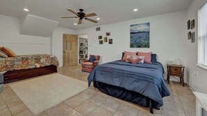 A bedroom with a large bed, a smaller bed, a chair, a bookshelf, and a ceiling fan.