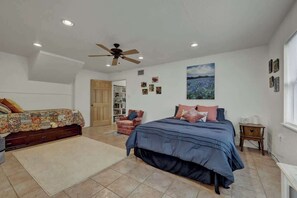A bedroom with a large bed, a smaller bed, a chair, a bookshelf, and a ceiling fan.