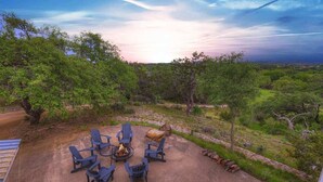 An outdoor patio with blue chairs and a fire pit, surrounded by lush greenery and a scenic view.