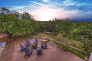 Un patio al aire libre con sillas azules y una chimenea, rodeado de exuberante vegetación y una vista panorámica.