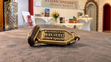 Ein mit 'Weinhotel Wachau' gravierter Messing-Schlüssel liegt auf einem Teppichboden in einer Hotelhalle mit einer Kristallleuchter und einem Schild mit der Aufschrift 'Stierschneider's Weinhotel Wachau'.