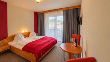 A hotel room with a bed, a table with a wine glass and bottle, and a TV on the wall.