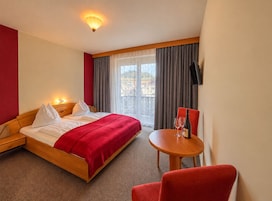 A hotel room with a bed, a table with a wine glass and bottle, and a TV on the wall.