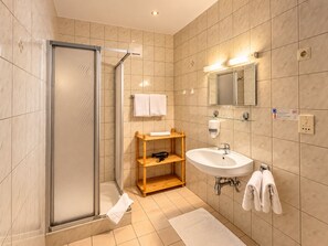 Un baño moderno con ducha envuelta en vidrio, un estante de madera, un lavamanos y un espejo.
