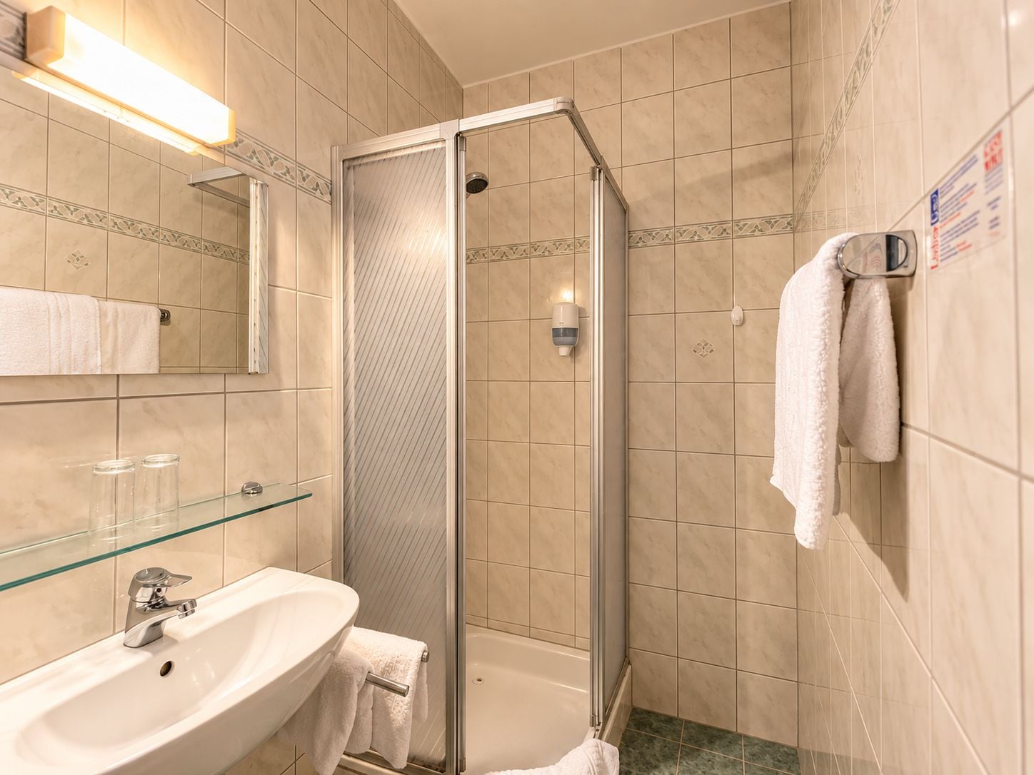 A bathroom with a glass-enclosed shower, a sink with a mirror, and a towel rack.