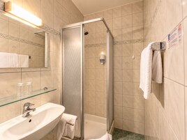 Casa de banho com chuveiro em cabine de vidro, pia com espelho e porta-toalhas.