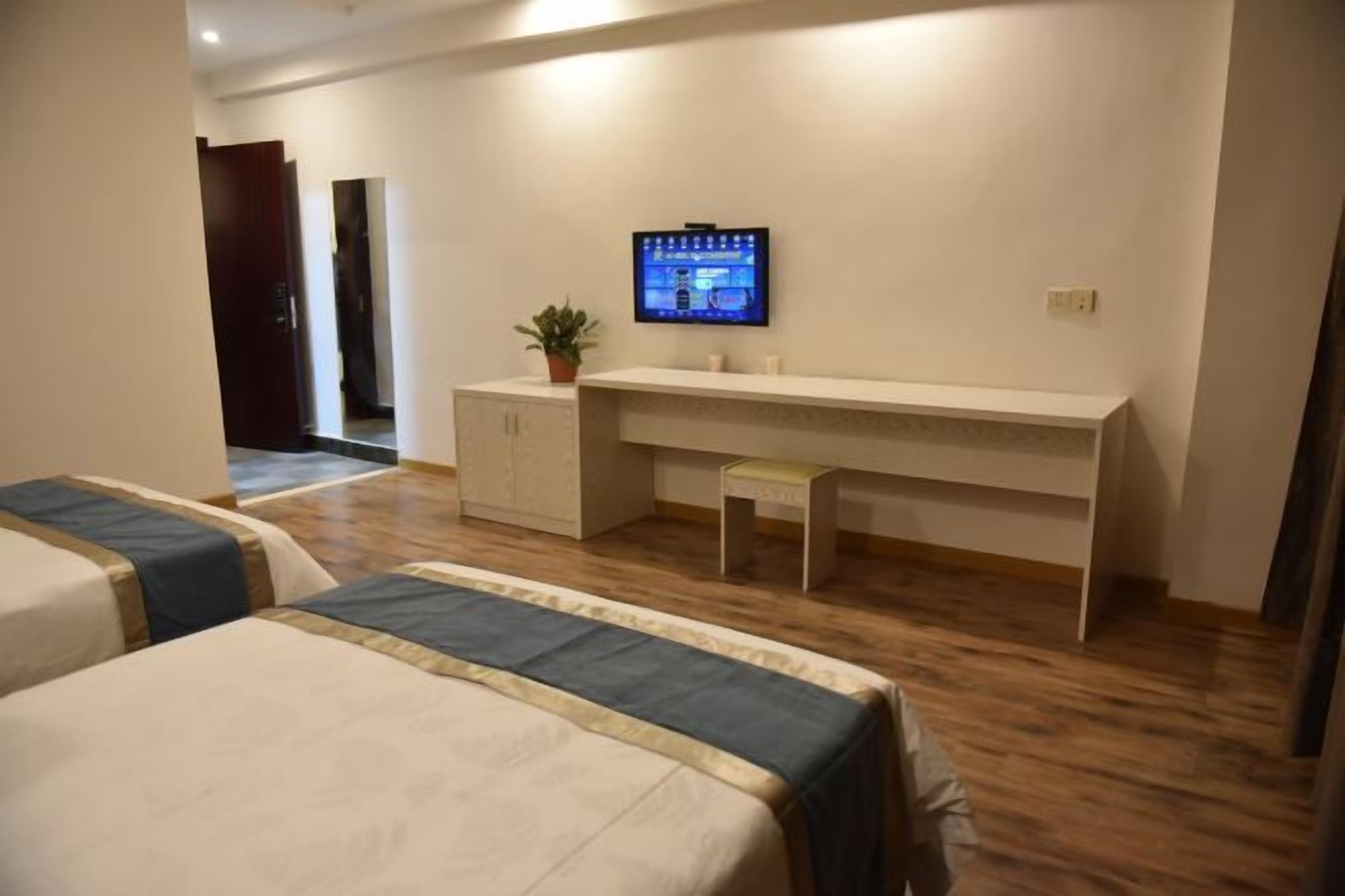 Habitación de hotel con dos camas, un escritorio con televisor, una planta pequeña y un armario.