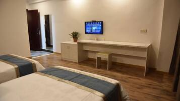 Habitación de hotel con dos camas, un escritorio con televisor, una planta pequeña y un armario.