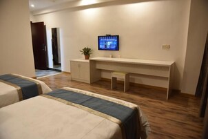 Habitación de hotel con dos camas, un escritorio con televisor, una planta pequeña y un armario.