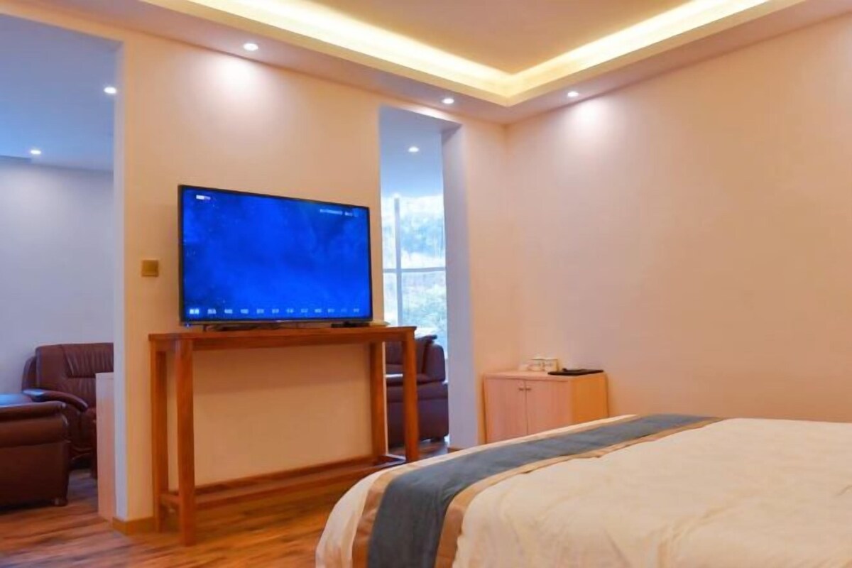 Quarto de hotel com cama, televisão sobre suporte, área de estar e janela.