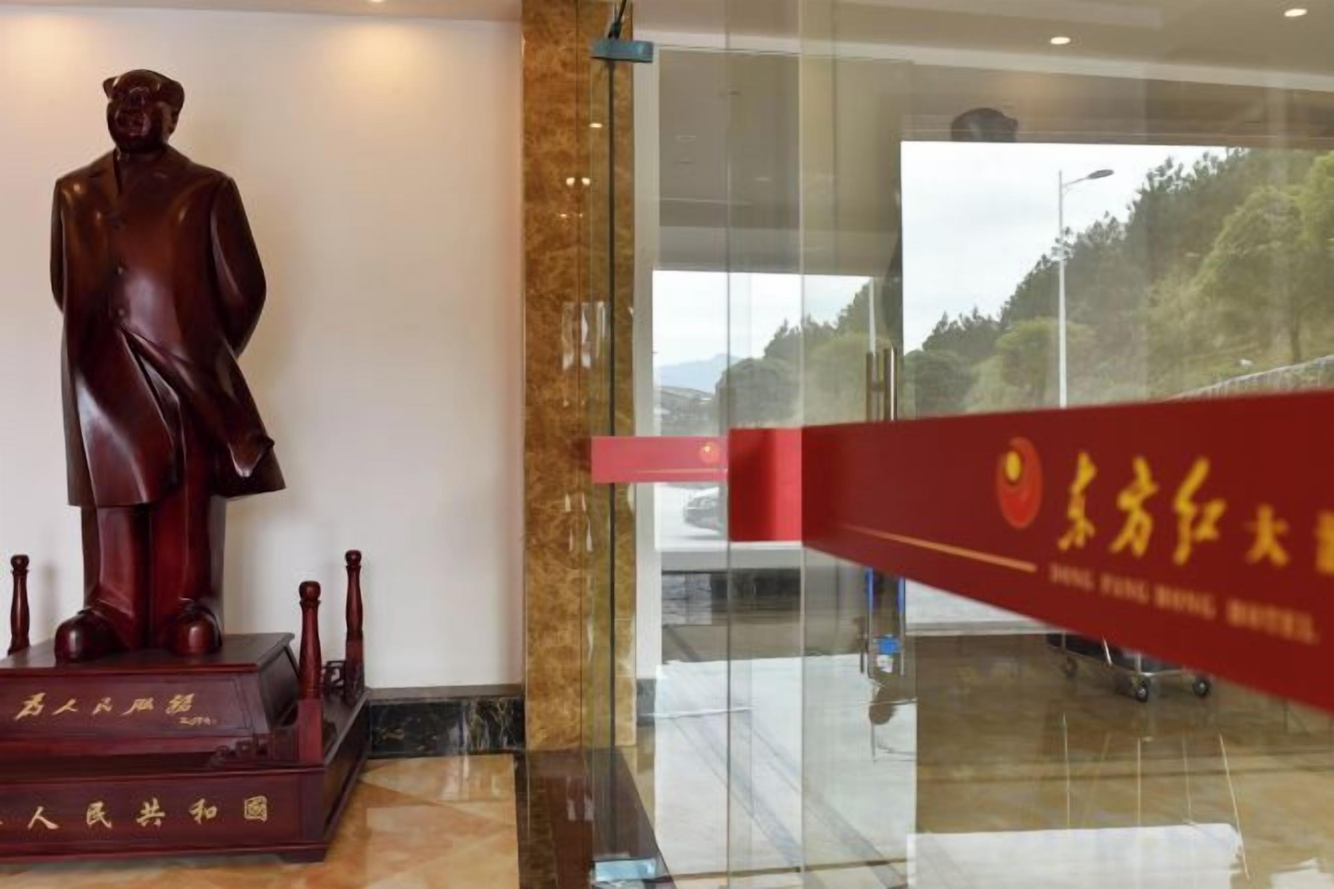 A statue of a man in a suit, a red banner with Chinese characters, and a glass door leading to a view of trees.