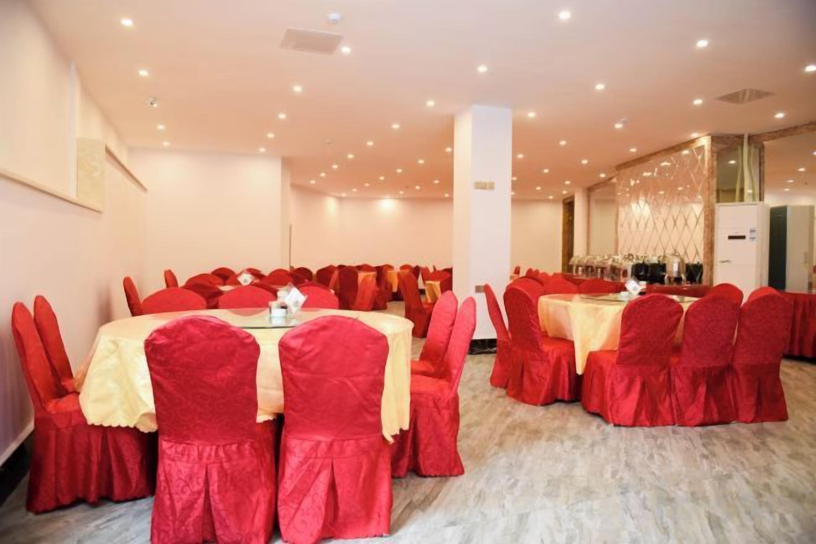 A banquet hall with round tables and red chairs, a marble floor, and a modern chandelier.