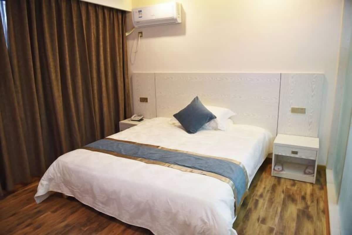 Quarto de hotel com cama, mesa de cabeceira, ar-condicionado fixado na parede e piso de madeira.