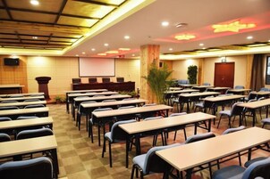 Un salón de conferencias con varias mesas y sillas, una pantalla de proyector y un atril.