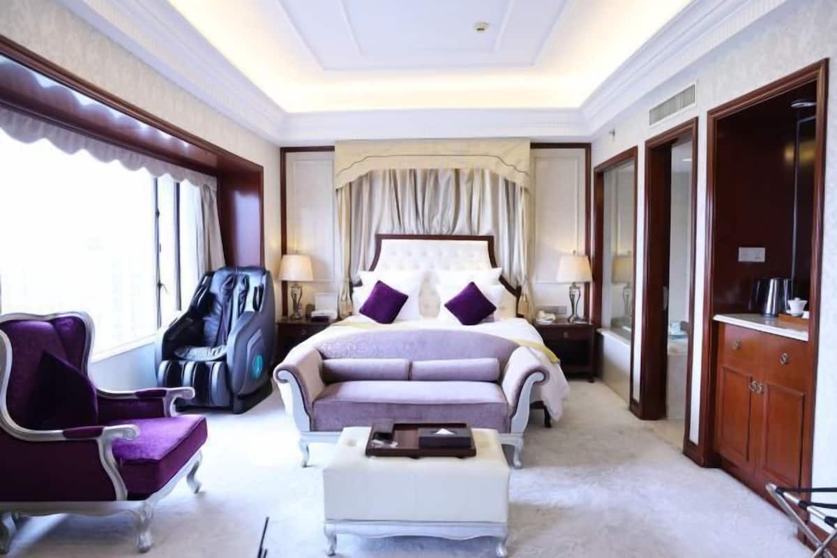 A hotel room with a large bed, a chaise lounge, a massage chair, and a wooden wardrobe.