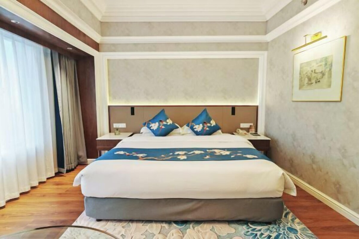 Een hotelkamer met een groot bed, een nachtkastje en een prentje in een lijst aan de muur.