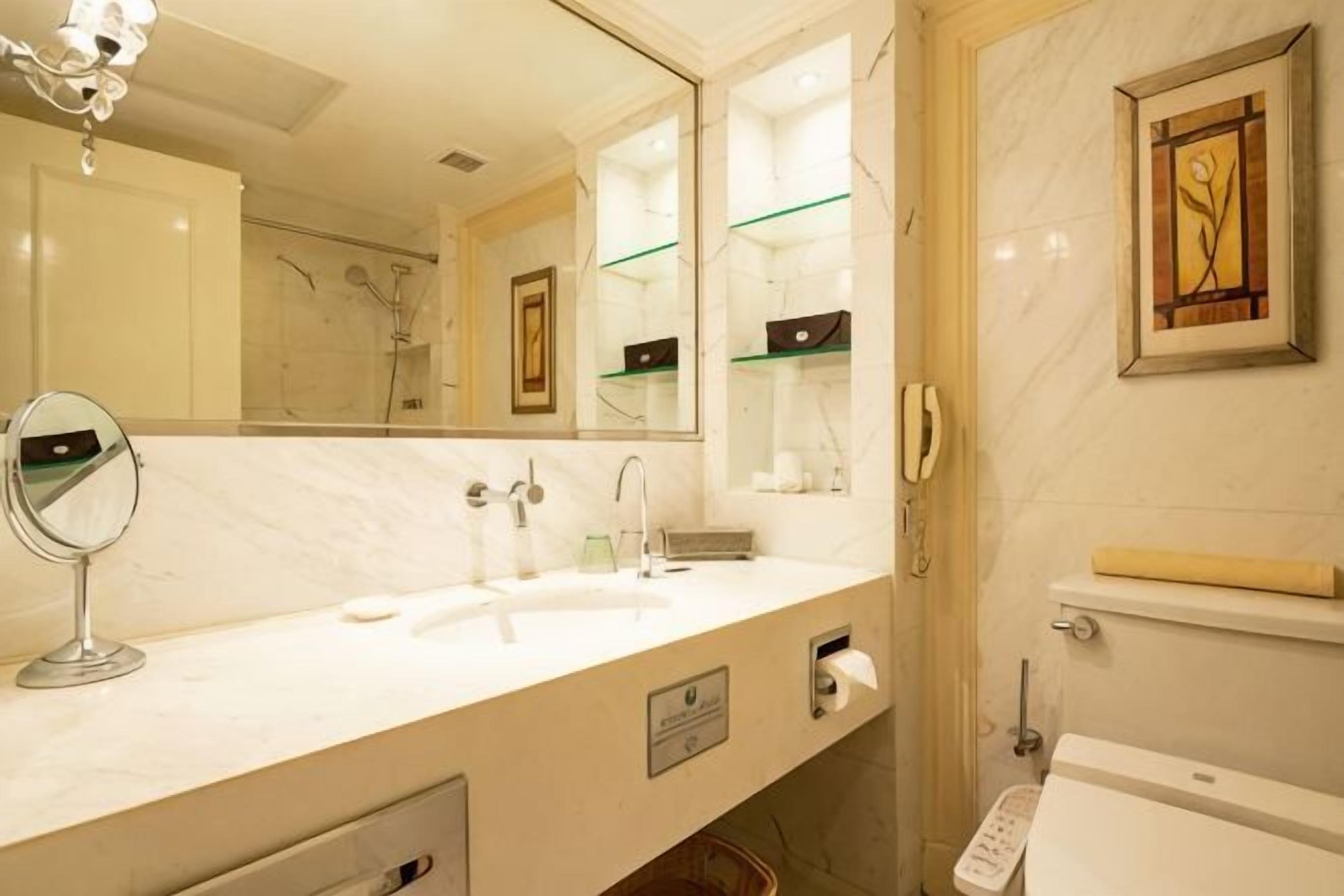 A bathroom with a marble sink, a mirror, a toilet, and a framed artwork on the wall.