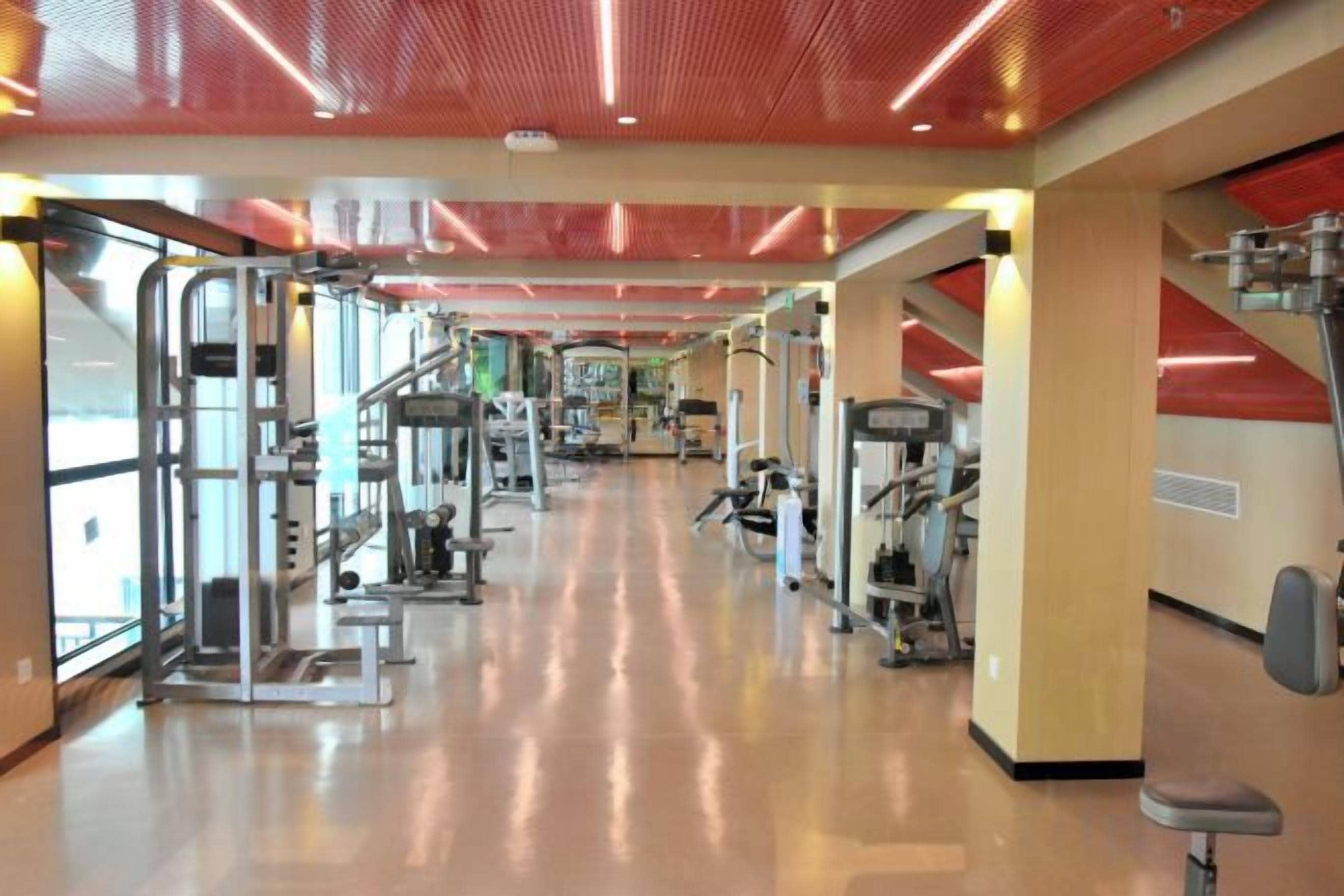 Une salle de sport équipée de matériel d’exercice, dotée d’un mur miroir et d’un plafond rouge.