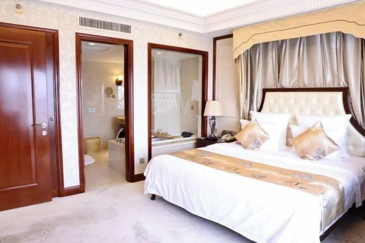 A hotel room with a large bed, a bathroom with a mirror, and a door leading to another room.