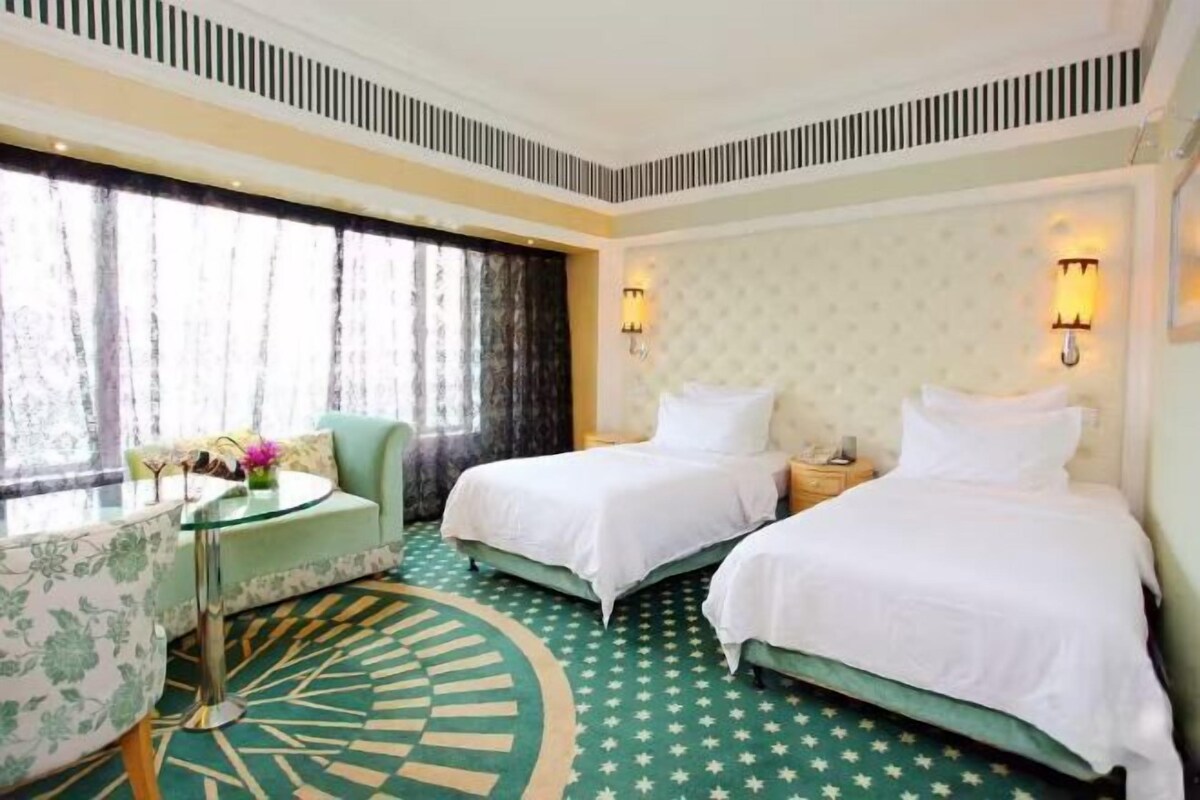 Een hotelkamer met twee bedden, een ronde tafel met stoelen, een raam met gordijnen en een kamerbreed tapijt met patroon.