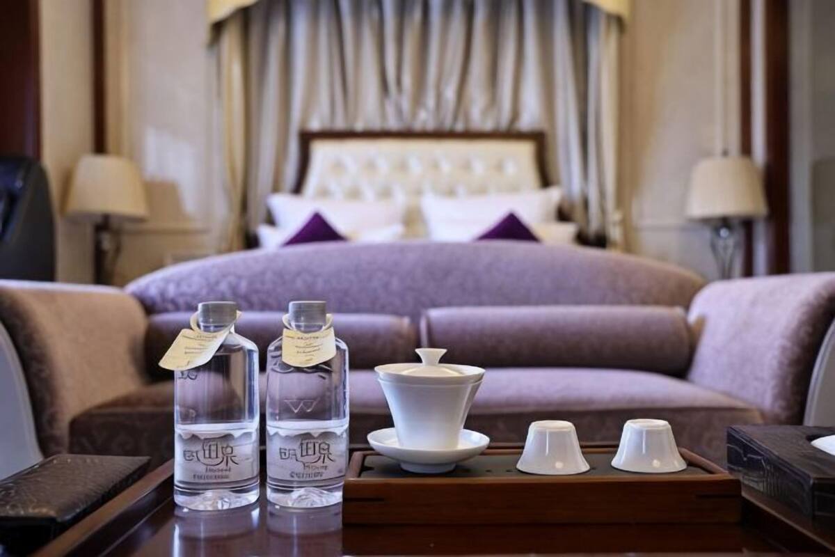 A hotel room with a bed, a sofa, a table with water bottles, a teapot, and cups.