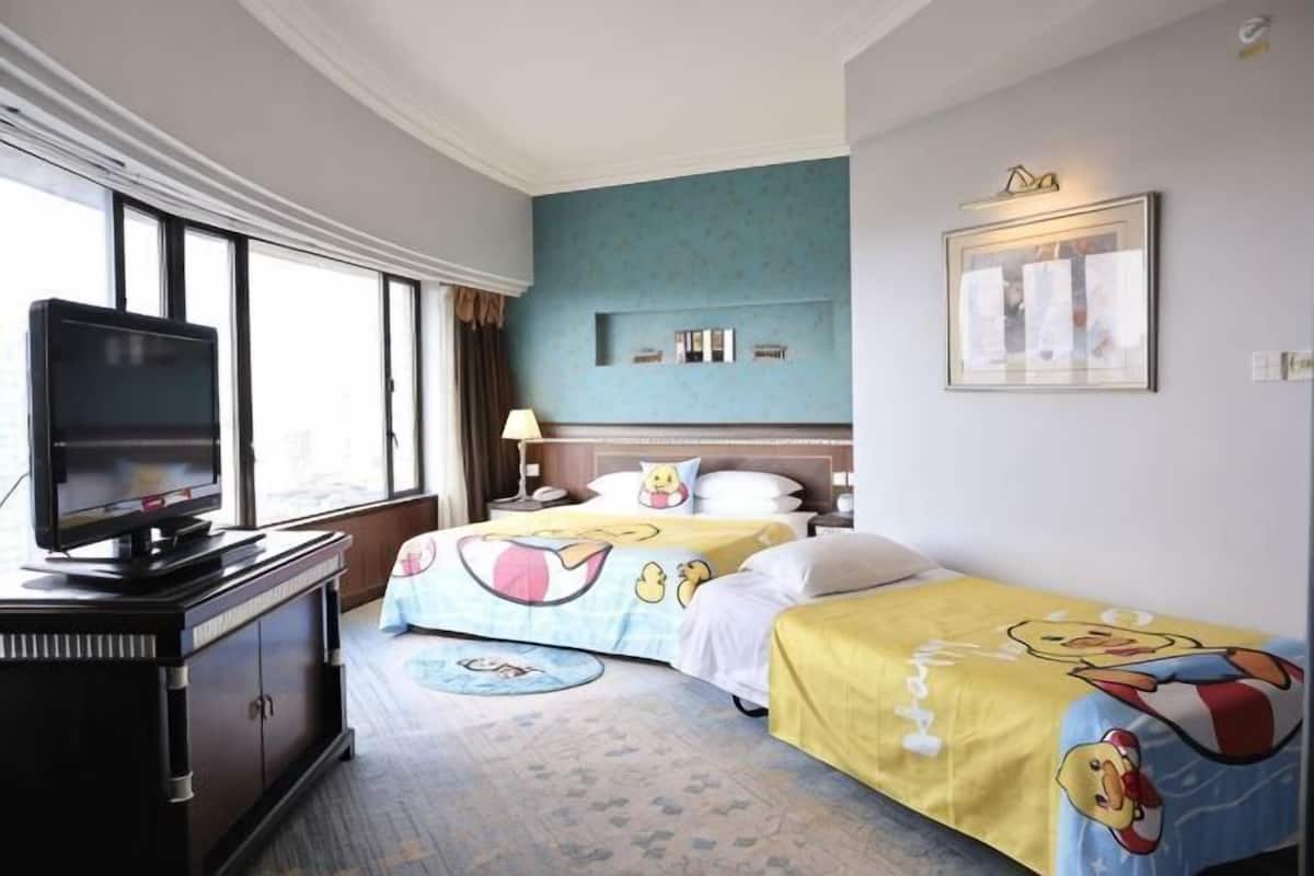 A hotel room with two beds, a television, a desk, and a window.