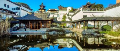 A traditional courtyard with a pond reflecting buildings, a pavilion, and a small bridge.