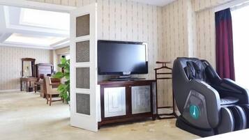 A living room with a television, a massage chair, a dining area, and a plant.