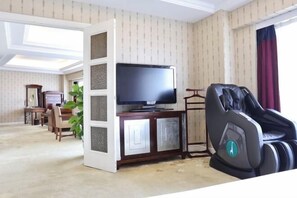 Sala de estar con televisor, sillón de masaje, comedor y una planta.