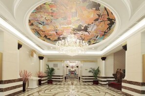 Een statig atrium met een grote muurschildering aan het plafond, een kroonluchter en een marmeren vloer.