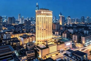 A high-rise hotel with a prominent sign, surrounded by a dense urban cityscape at dusk.