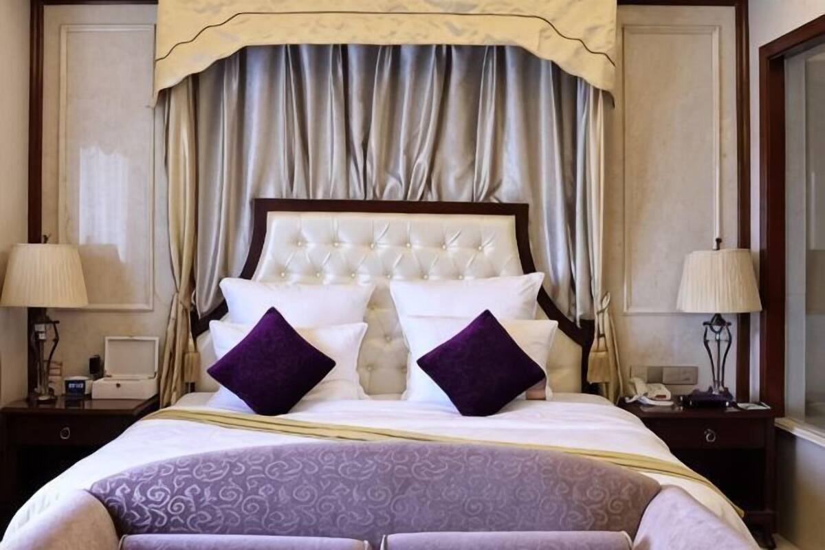 A hotel room with a large bed, two bedside lamps, a nightstand, and a window with curtains.
