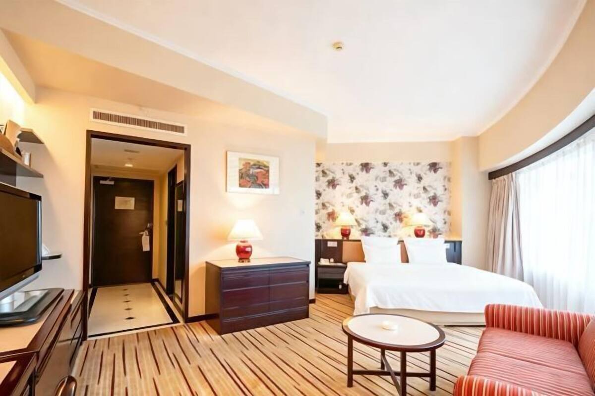 A hotel room with a bed, a TV, a desk, a sofa, and a wall with a floral pattern.
