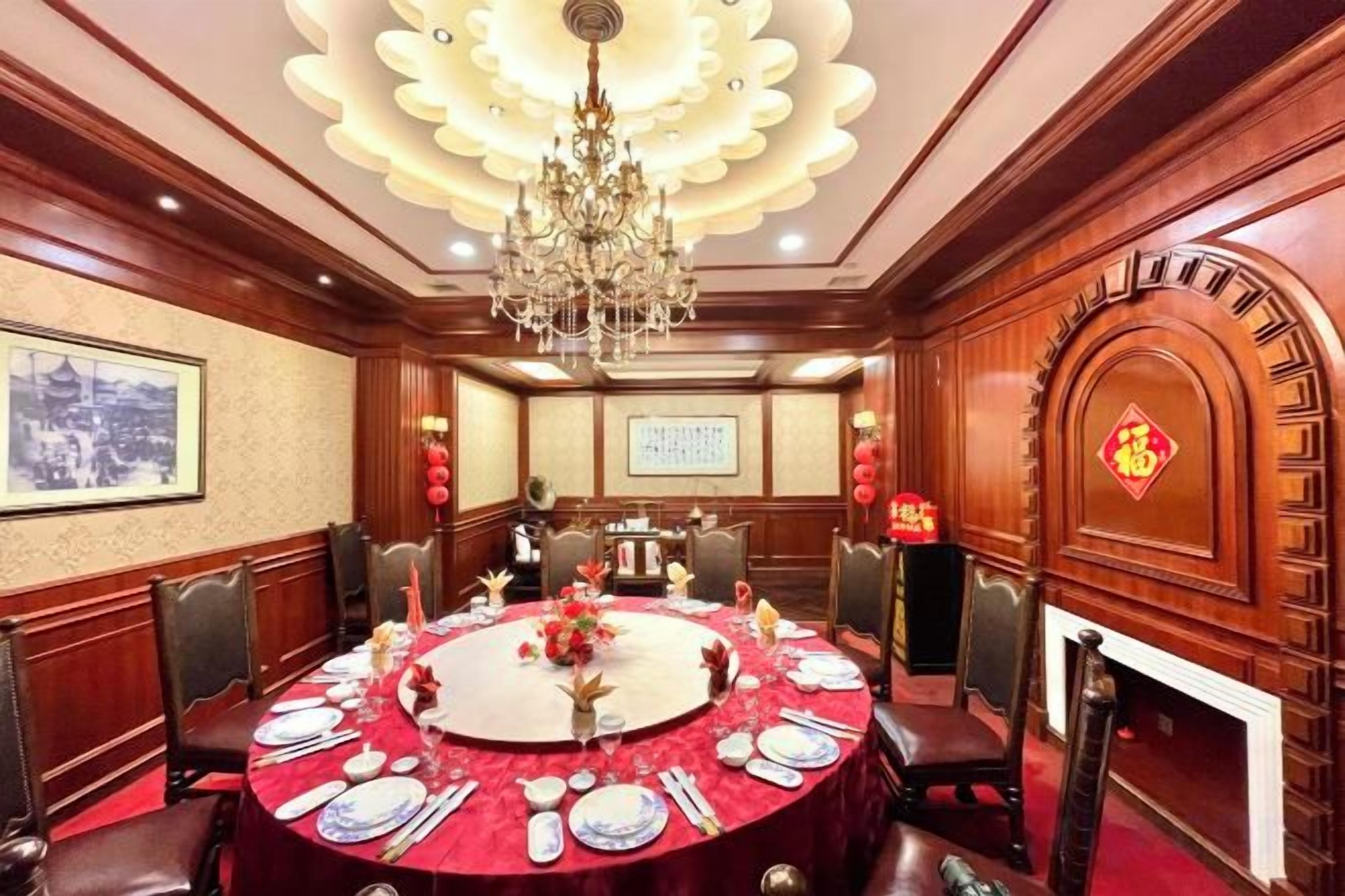 A conference room with a round table set for a meeting, surrounded by chairs, a chandelier, and traditional decor.