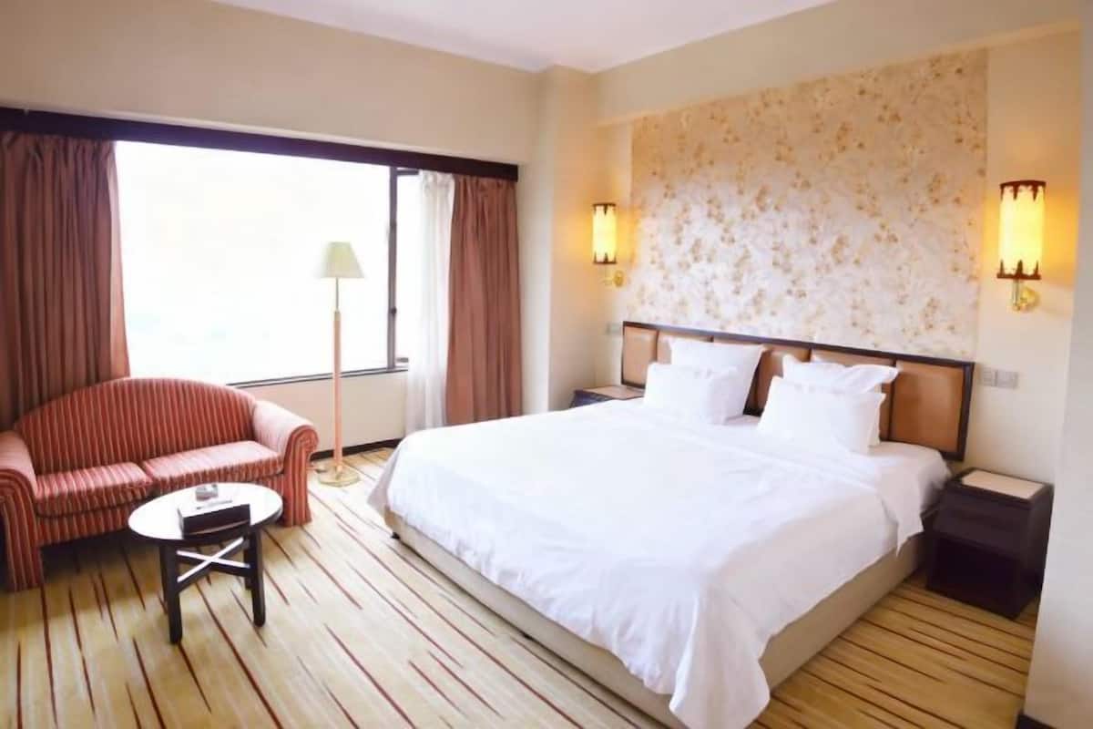 A hotel room with a large bed, a sofa, a small table, and two wall-mounted lamps.
