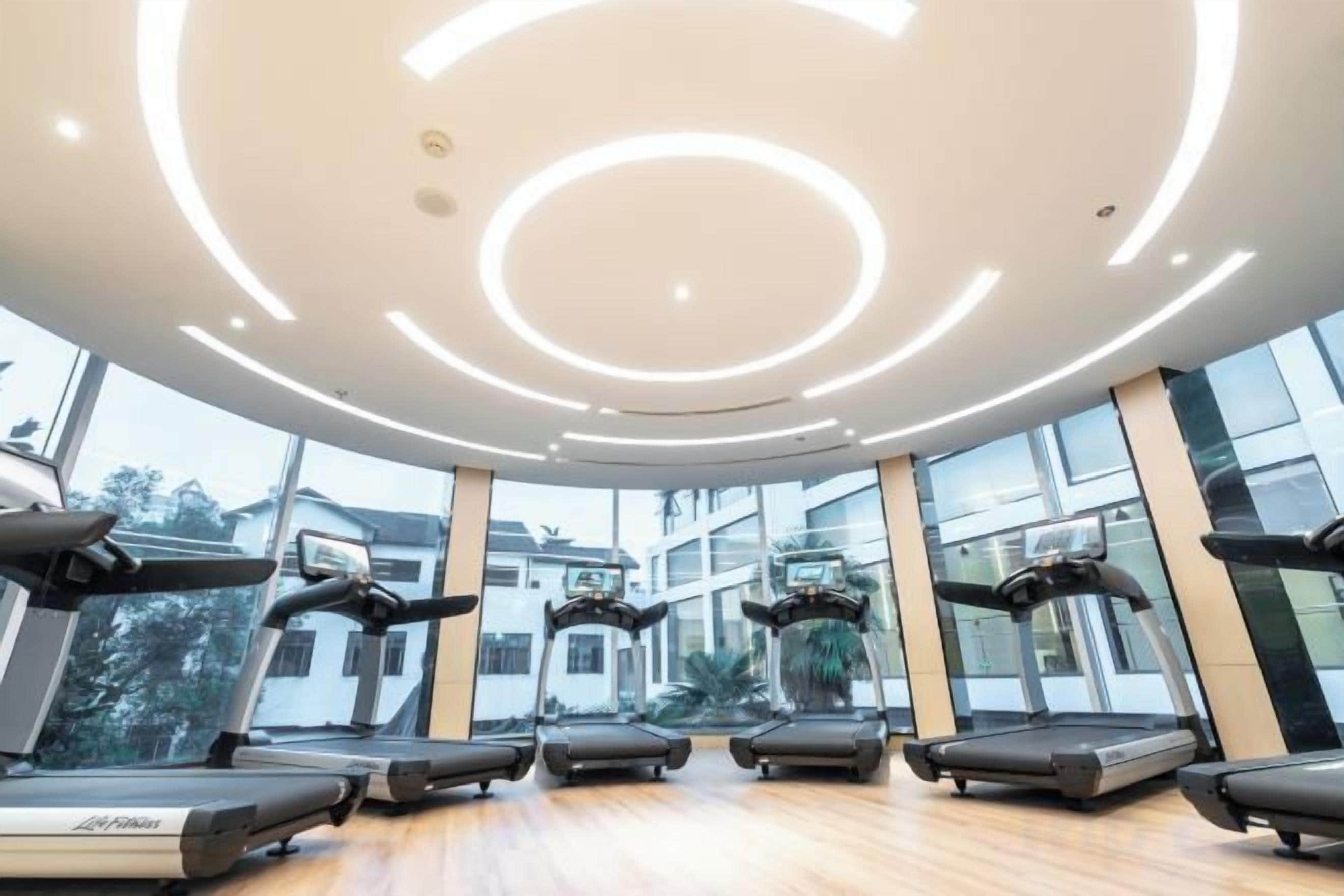 A modern gym with treadmills, large windows, and a circular light design on the ceiling.