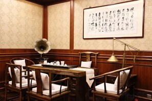 Ett traditionellt japanskt rum med tatamimattor på golvet, ett lågt träbord och stolar. På väggen hänger en inramad kalligrafisk tavla, och det finns en golvlampa.