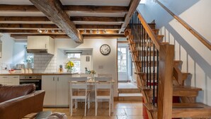 Un'ampia zona giorno con una scala in legno, un tavolo da pranzo con sedie e una cucina sullo sfondo.