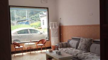 A room with a sofa, a small table, and a chair near a window with a view of a car outside.