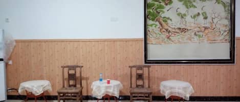 Una habitación con un panel de madera en la pared, un cuadro grande enmarcado y cuatro sillas con cubre individuales de encaje.