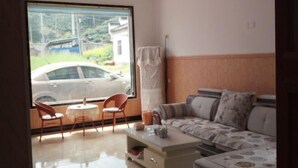 A room with a sofa, a small table, and two chairs near a window with a view of a car and greenery outside. - Loushanqiao Homestay No.2 (Shitai)