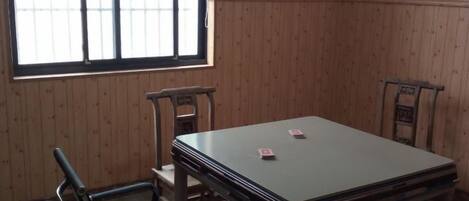 A room with a wooden paneled wall, a table with chairs, and a window with bars.