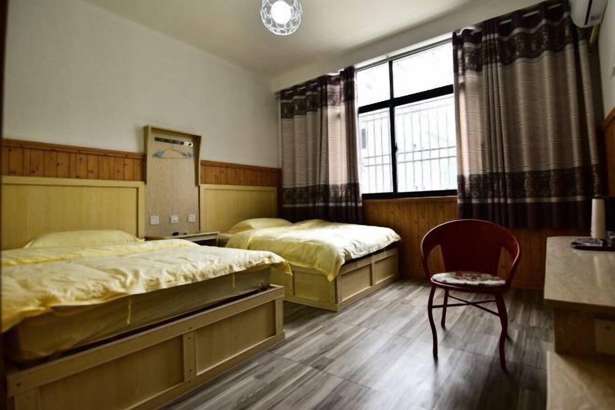 Ein Zimmer mit zwei Betten, einem Sessel, einem Schreibtisch und einem fenster mit Vorhängen.