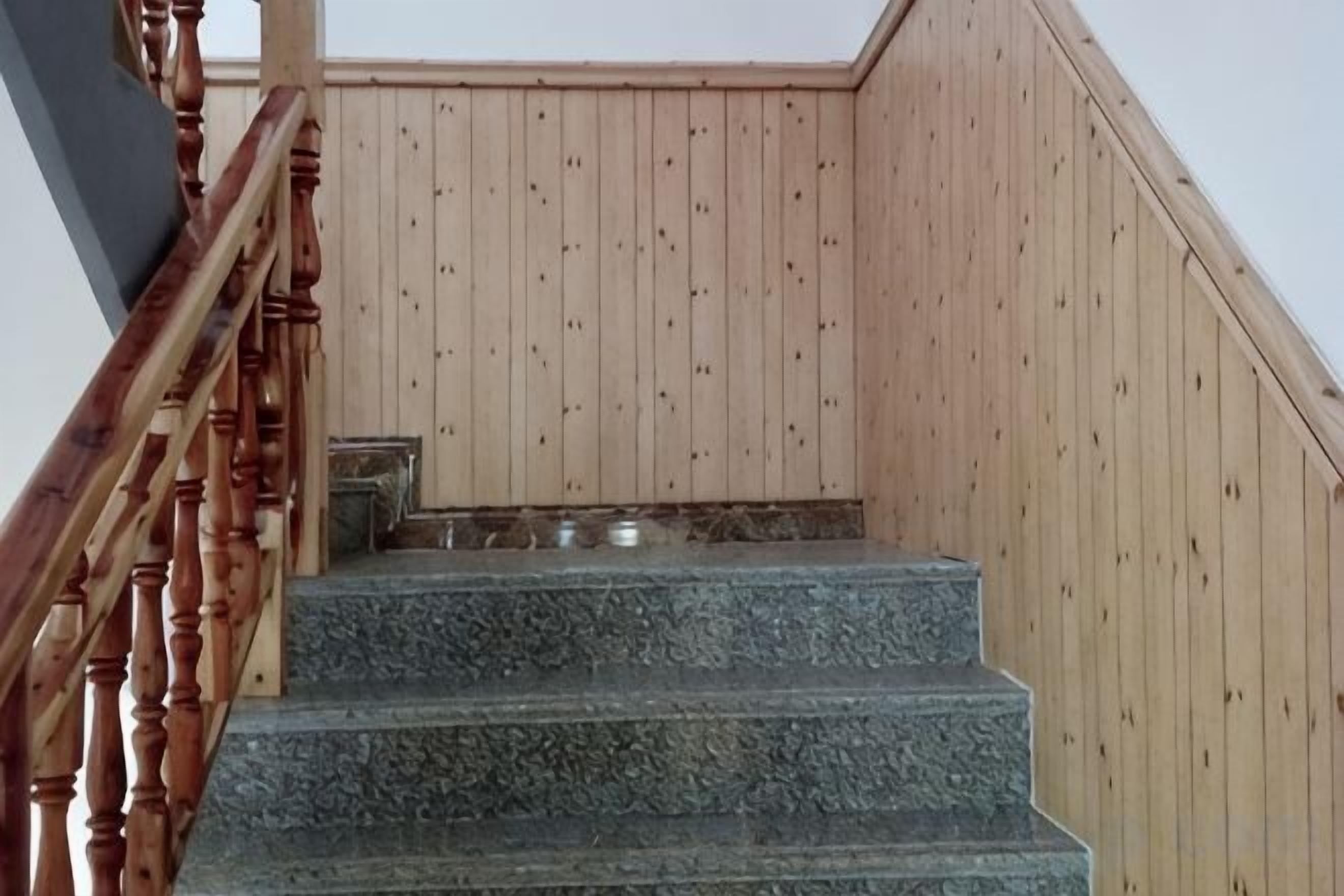 A wooden staircase with a handrail, leading to a landing with a metal bench.