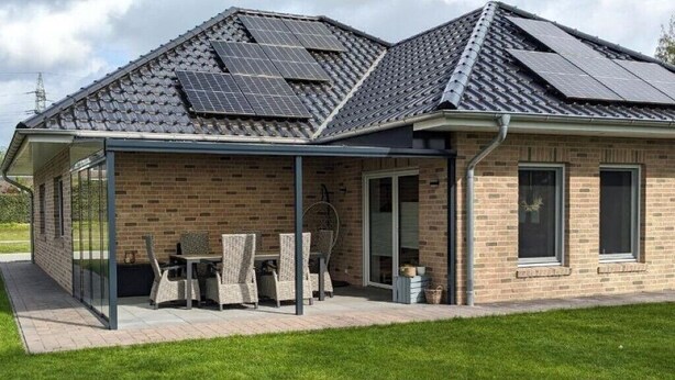 Une maison dotée d’un patio couvert, de panneaux solaires sur le toit et d’une façade en briques.