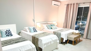 A hotel room with two beds, a small seating area, and a window with curtains. - Pousada Praia By Bia (Penha)