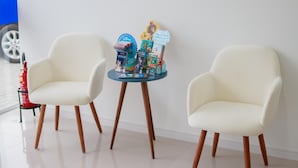 Two white armchairs with wooden legs, a small round table with a blue top, and a wall-mounted decoration. - Pousada Praia By Bia (Penha)