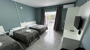 A hotel room with two single beds, a desk with a chair, a flat-screen TV, and a large window with curtains. - Pousada Praia By Bia (Penha)