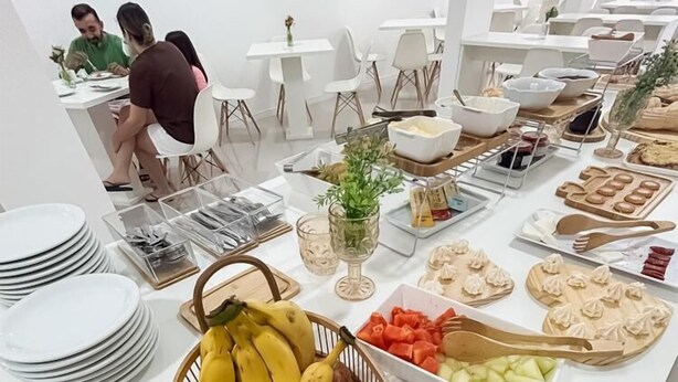 A buffet setup with various fruits, pastries, and a dining area with white chairs and tables. - Pousada Praia By Bia (Penha)